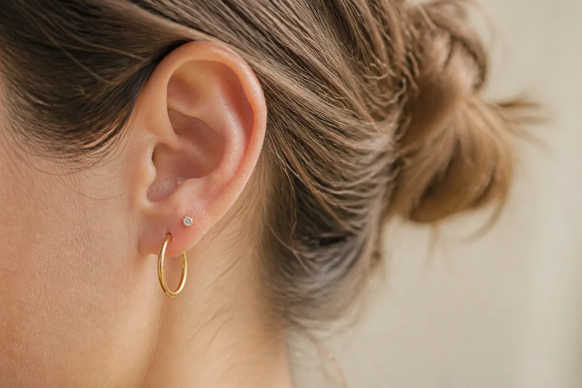 Cadrage serré de profil sur un lobe portant une créole fine, chignon relevé, visage hors champ